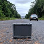 Tornozeleira eletrônica rompida em rodovia na fronteira Brasil-Paraguai, com viatura da PRF ao fundo.