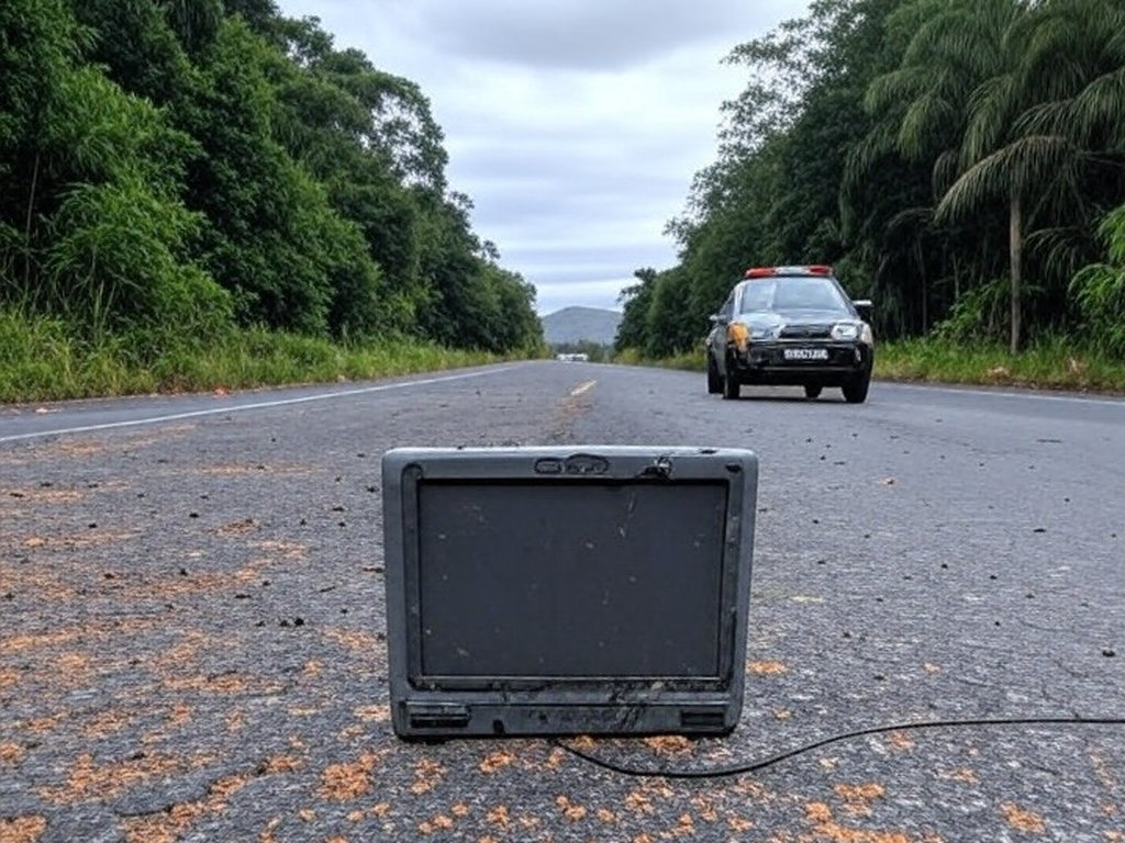 Tornozeleira eletrônica rompida em rodovia na fronteira Brasil-Paraguai, com viatura da PRF ao fundo.