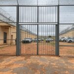 Vista externa de presídio no DF com portões e viaturas policiais, representando retorno de presos após saidão de Natal.