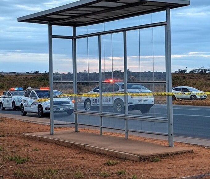 Parada de ônibus na DF-150 com fita de isolamento policial e viaturas da PMDF, cena de investigação em rodovia no Distrito Federal.