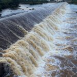 Represa do Descoberto transbordando, com águas inundando margens no DF, alertando para riscos de enchentes.