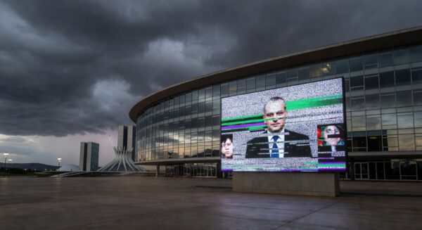 Fachada da CLDF em Brasília com símbolos de lentidão legislativa e falhas em transmissão ao vivo.
