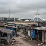 Favela em Brasília com moradias precárias e cruz católica ao fundo, expondo déficit habitacional e homenagem na CLDF.