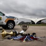 Viatura da Polícia Legislativa da CLDF em estádio esportivo vazio em Brasília, com troféus no chão, representando desperdício de recursos.