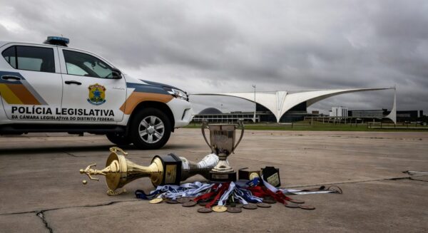 Viatura da Polícia Legislativa da CLDF em estádio esportivo vazio em Brasília, com troféus no chão, representando desperdício de recursos.