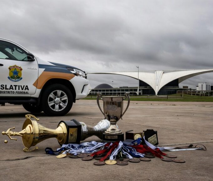 Viatura da Polícia Legislativa da CLDF em estádio esportivo vazio em Brasília, com troféus no chão, representando desperdício de recursos.