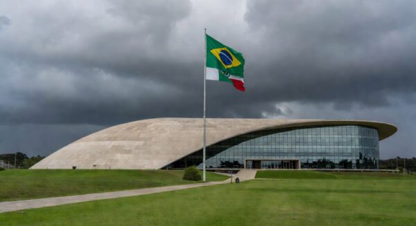 Edifício da CLDF em Brasília com documentos espalhados, representando atraso na regulamentação de lei antissupremacista.