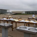 Evento em Brasília com bebedouros e documentos burocráticos, ilustrando novas obrigações aprovadas pela CLDF.
