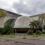 Edifício da CLDF em Brasília com documentos de seguros simbolizando críticas por fraudes e burocracias.