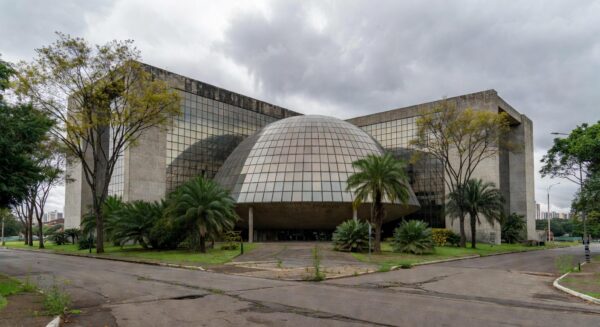 Edifício da CLDF em Brasília com documentos de seguros simbolizando críticas por fraudes e burocracias.