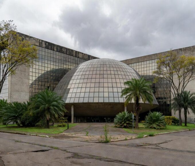 Edifício da CLDF em Brasília com documentos de seguros simbolizando críticas por fraudes e burocracias.