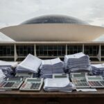 Imagem da Câmara Legislativa do DF com documentos fiscais simbolizando crítica à carga tributária excessiva.
