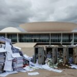 Edifício da CLDF em Brasília com pilhas de documentos e cofres sobrecarregados, representando ameaça aos cofres públicos do DF.