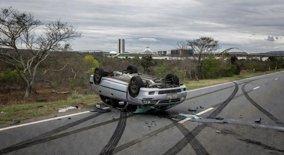 Carro capotado em acidente na DF-005 em Brasília, com destroços na rodovia e vegetação do cerrado ao fundo.