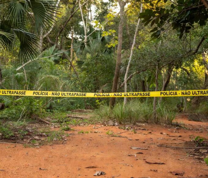 Cena de crime isolada com fita policial em floresta brasileira no Distrito Federal, representando denúncia por latrocínio e ocultação de cadáver.