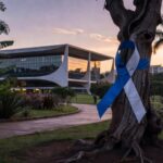 Fita azul e branca de conscientização sobre ELA em árvore de parque brasileiro, simbolizando luto por vítima da doença.