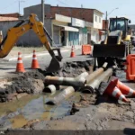 Obras de drenagem da Caesb em rua de São Sebastião com equipamentos e água acumulada