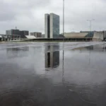 Ruas de Brasília molhadas pela chuva pontual, com edifícios ao fundo.