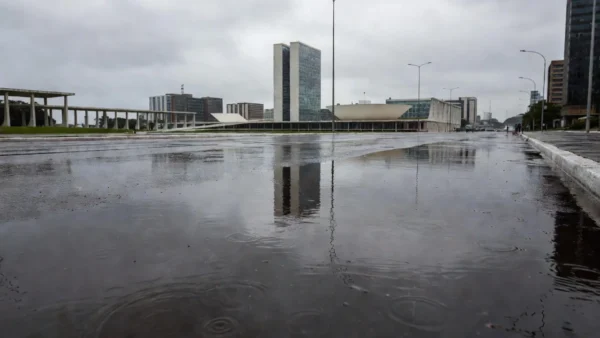 Ruas de Brasília molhadas pela chuva pontual, com edifícios ao fundo.