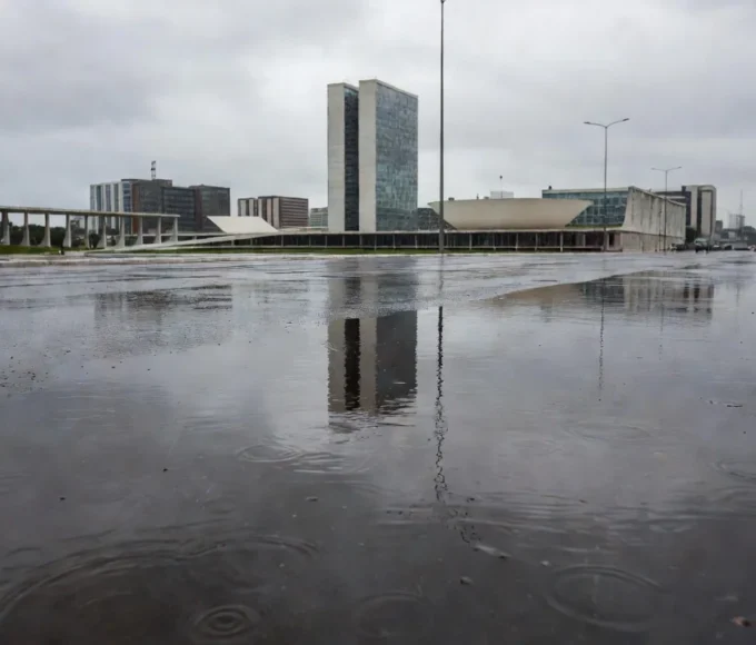 Ruas de Brasília molhadas pela chuva pontual, com edifícios ao fundo.