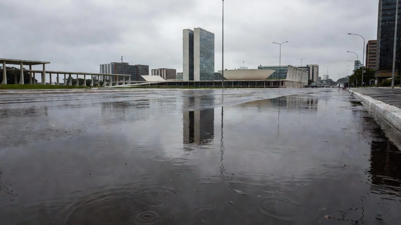 Ruas de Brasília molhadas pela chuva pontual, com edifícios ao fundo.